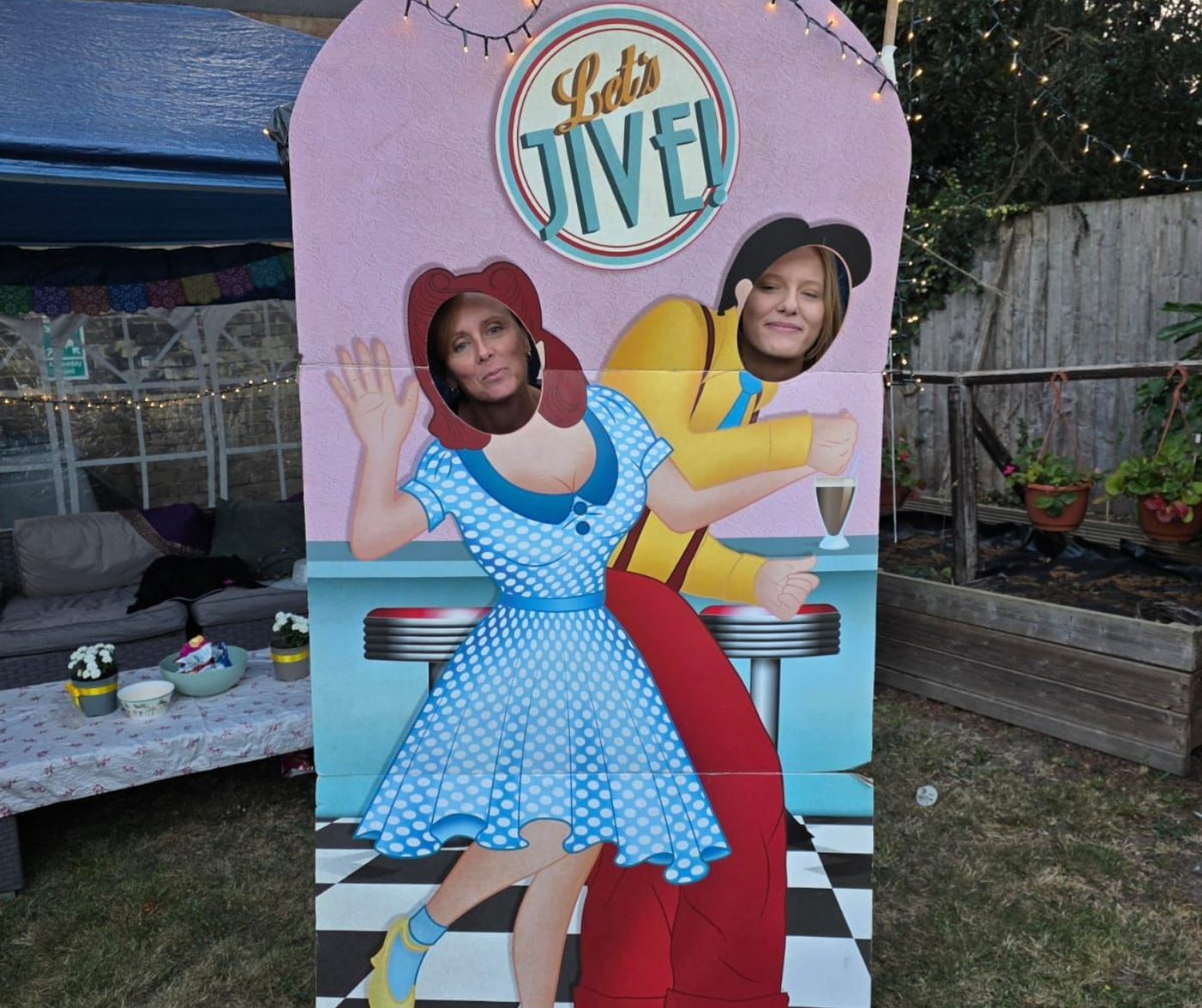 two women putting their faces through a wooden frame that has painted bodies of 50's style dancers